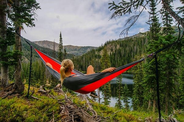 Woman lying in a hammock in the middle of the woods overlooking a lake.