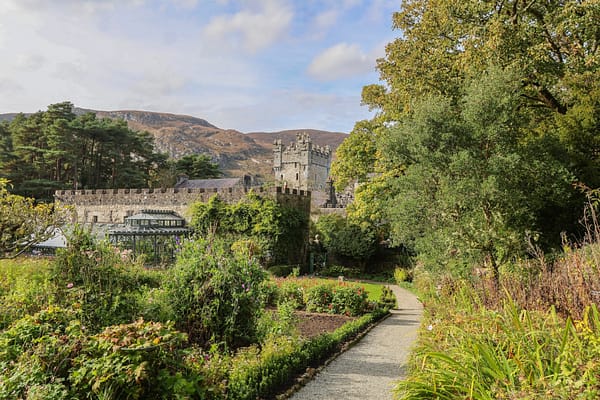 Glenveagh Castle & Gardens A lush green garden with flowers and trees with Glenveagh Castle and mountains in the background.