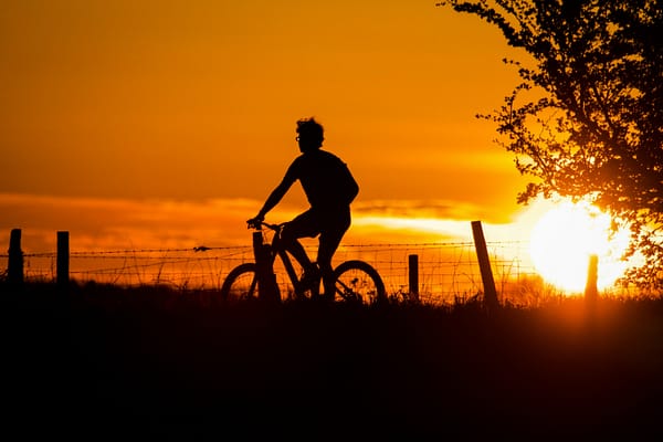 Silhouette of an individual cycling at sunset.