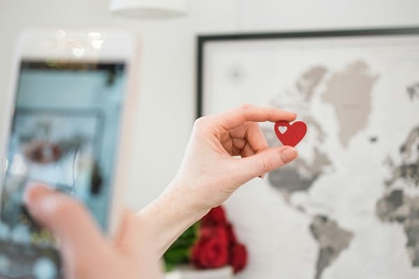 Hand holding up a red heart in front of a framed map.