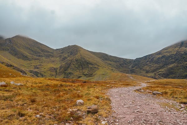 Towards Carrauntoohil Stone path winding through fields towards the steep, rocky ascent of the Devil's Ladder, a popular ascent for climbing Carrauntoohil.