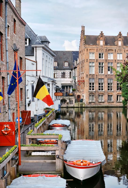 Belgium Despina Galani - Unsplash Canal in Belgium with EU and Belgium flags.